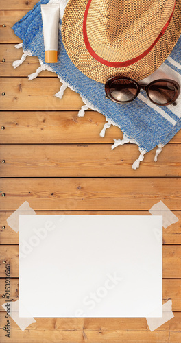 Summer Wallpaper with Straw Hat, Towel, Sunglasses, Protection Cream and White Blank Free Space Paper Sheet with Adhesive Tape on Wood Planks Surface. File with Clipping Path.