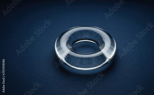 Transparent crystal glass torus shape optical lens or paperweight on a dark blue textured background representing physics and modern design