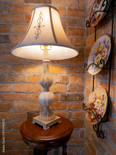An illuminated antique lamp on a wood table next to a brick wall