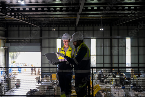 Engineers discussing factory automation on laptop in industrial warehouse