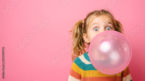 Surprised little girl blowing a big pink bubblegum bubble on a pink background representing playful childhood fun, sweet candy snack, and vibrant pop art humor.