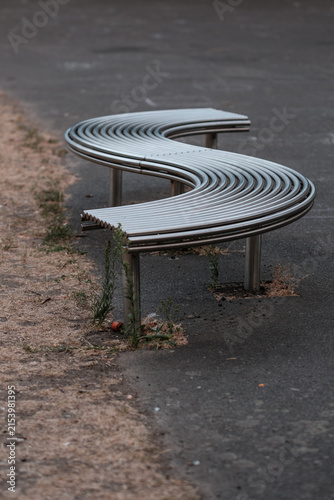 Canvas Print Modern s-shaped metal bench on urban street pavement