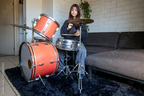 Fotografie A hispanic teenage girl practices the drums at home