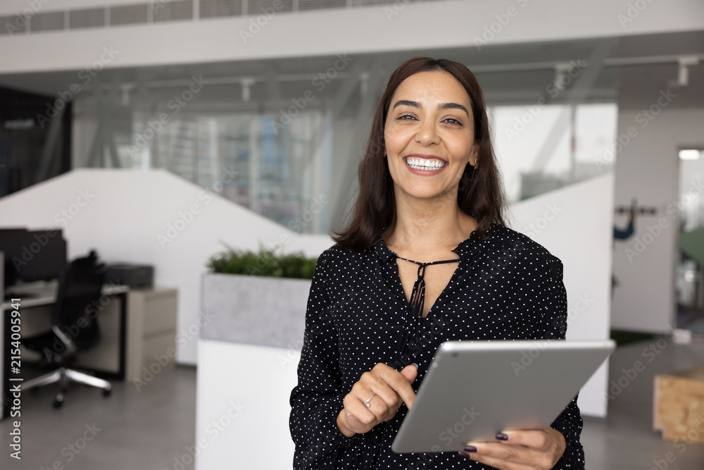 Fototapeta premium Portrait of Arabian businesslady, marketing specialist or project manager posing in office with tablet, looking at camera, exuding professionalism and authority. Modern tech, digital communication