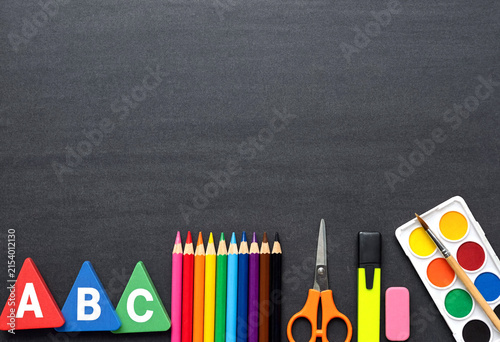 Colorful educational supplies including alphabet blocks pencils scissors and watercolor paints on dark background