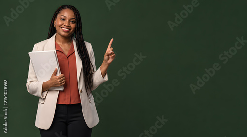 Businesswoman holding a white folder while pointing to empty copy space against a dark green studio wall backdrop during a corporate photoshoot.