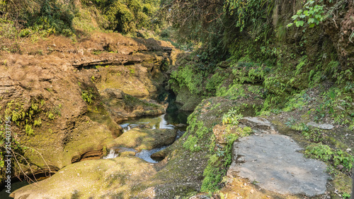 The stream winds through a narrow crevice in the rocks. There are moss and green plants on cliffs. Nepal. Pokhara. Davis Falls