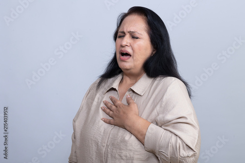 Принти на полотні Mature Indian woman holding her chest while experiencing apparent chest pain and discomfort, showing a distressed expression in a clean studio setting, representing a health and medical concern