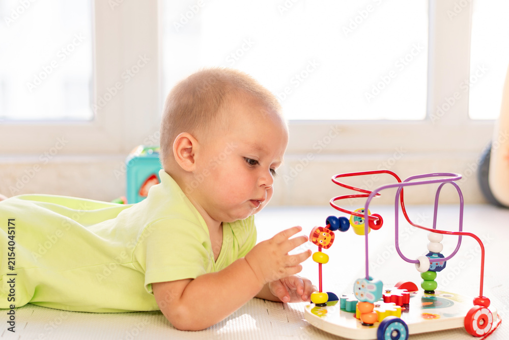 Naklejka premium Baby Boy Reaches For Beads On Educational Maze Toy