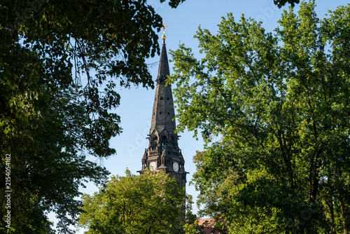 Konstfotografi Garnison Church St Martin Dresden steeple framed by vibrant green trees under a clear blue sky on a sunny day