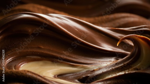 Macro of swirling milk and dark chocolate mixture creating a smooth wavy pattern with glossy highlights on a dark brown background