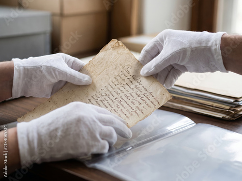 Historian wearing protective white gloves holding fragile vintage paper manuscript