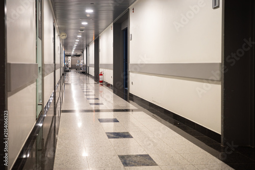 Fotografie Interior view of a quiet clinic hallway showing reflective floor tiles an emergency fire extinguisher and medical equipment carts parked in the distance creating a professional healthcare space