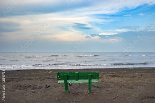 A lonely green bench on a sandy beach overlooking the ocean