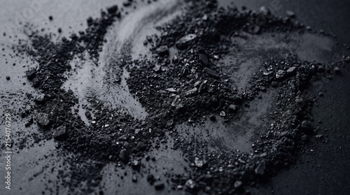 Black charcoal powder texture scattered on dark background for beauty and skincare concept.