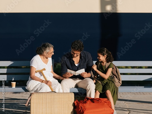 An Indian multigenerational family waits at a train station platform, featuring a grandmother with a cane and a man checking a paper ticket for travel and tourism concepts with copy space above