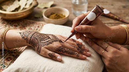 Woman gets intricate henna tattoo applied to hand with traditional design during cultural celebration close-up.