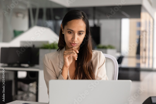 Fotografie Focused businesswoman working on project, reviewing digital data on laptop screen, analyzing, thinking on strategic business decisions, sit at workplace desk in corporate office
