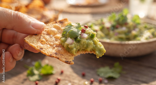 Foto A focus-stacked, mouth-watering image capturing a bite taken of a totopo loaded with chunky guacamole, highlighting the satisfying crunch of the chip against the smooth, creamy dip