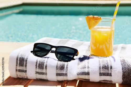 Relaxing by the Poolside: A Refreshing Drink, Sunglasses, and a Towel Await for a Perfect Summer Day