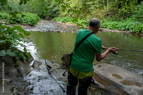 A man fishes with his dog on a scenic forest river in a pristine environment.