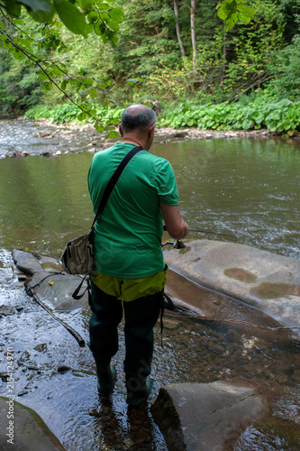 A man fishes with his dog on a scenic forest river in a pristine environment.