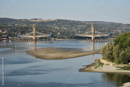 Aerial view of low river water level on the Danube in Novi Sad, Serbia, with suspended cargo ship navigation and new bridge construction in the distance