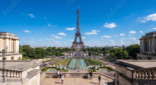 A breathtaking, high-resolution travel photograph of the majestic Eiffel Tower framed against a brilliant blue sky with soft white clouds, captured from the elevated terrace of Trocadéro. 