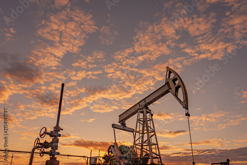 Oil Pumpjack and Wellhead Equipment Against Dramatic Sunset Sky