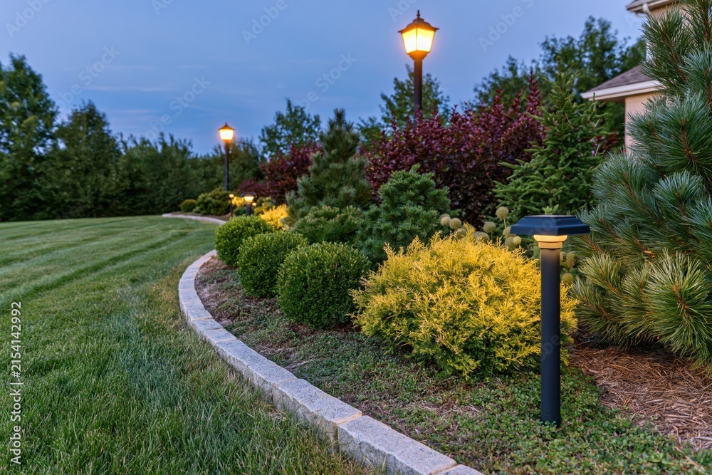 Obraz premium The Evening Garden Landscape With Curved Stone Border And Illuminated Lamps
