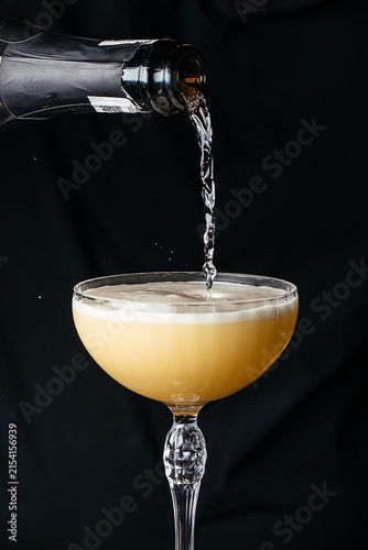 Champagne being poured into a crystal coupe glass with a frothy surface against a black background, highlighting the drink's golden hue and effervescence