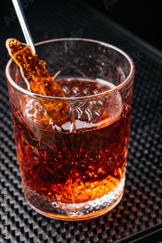 Obraz na plátně Close-up of a crystal glass filled with amber-colored beverage, ice cubes, and a