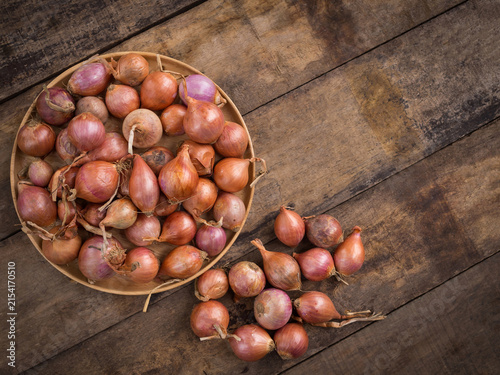 Fresh raw shallots in wooden plate on rustic dark wooden table with copy space.
