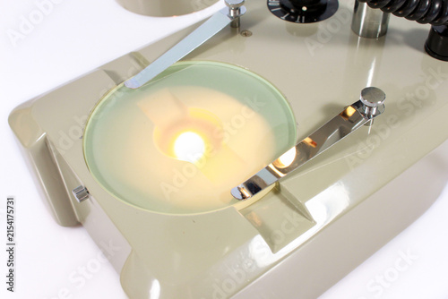 Close-up of a vintage microscope stage with built-in light, metal clips and mechanical controls for laboratory observation.