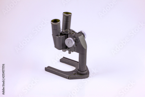 Old optical microscope with dual eyepieces, metal controls and a round glass stage for laboratory observation and research.
