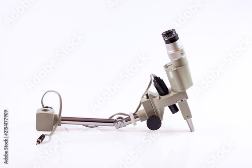 Vintage microscope head and support arm with eyepiece, focusing knob and electrical cable isolated on a white background.