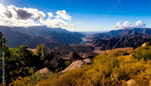 Panoramic view of a scenic mountain canyon landscape under a bright blue sky.