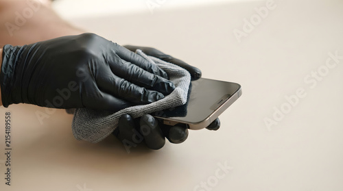 Gloved hands meticulously cleaning a smartphone screen with a microfiber cloth, emphasizing essential device hygiene and germ prevention for daily health