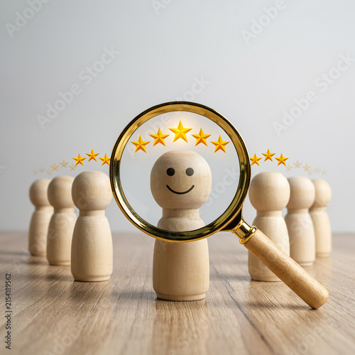 Wooden figure with a smiling face is examined through a magnifying glass for a high rating concept.