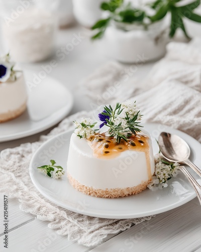 A delectable white cheesecake topped with passion fruit coulis and delicate edible flowers, presented on a white plate with a silver spoon and fork