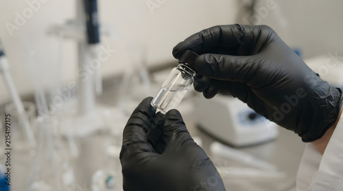 Gloved hands holding a small glass vial in a professional scientific laboratory for medical research