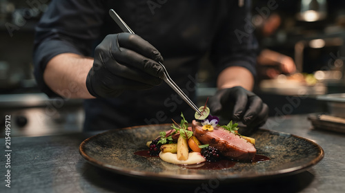 Professional Chef Using Precision Tweezers to Plate a High End Gourmet Meat Dish in a Modern Restaurant Kitchen