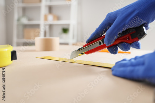Quadro su tela Hand in blue protective glove using a utility knife and ruler to cut material on