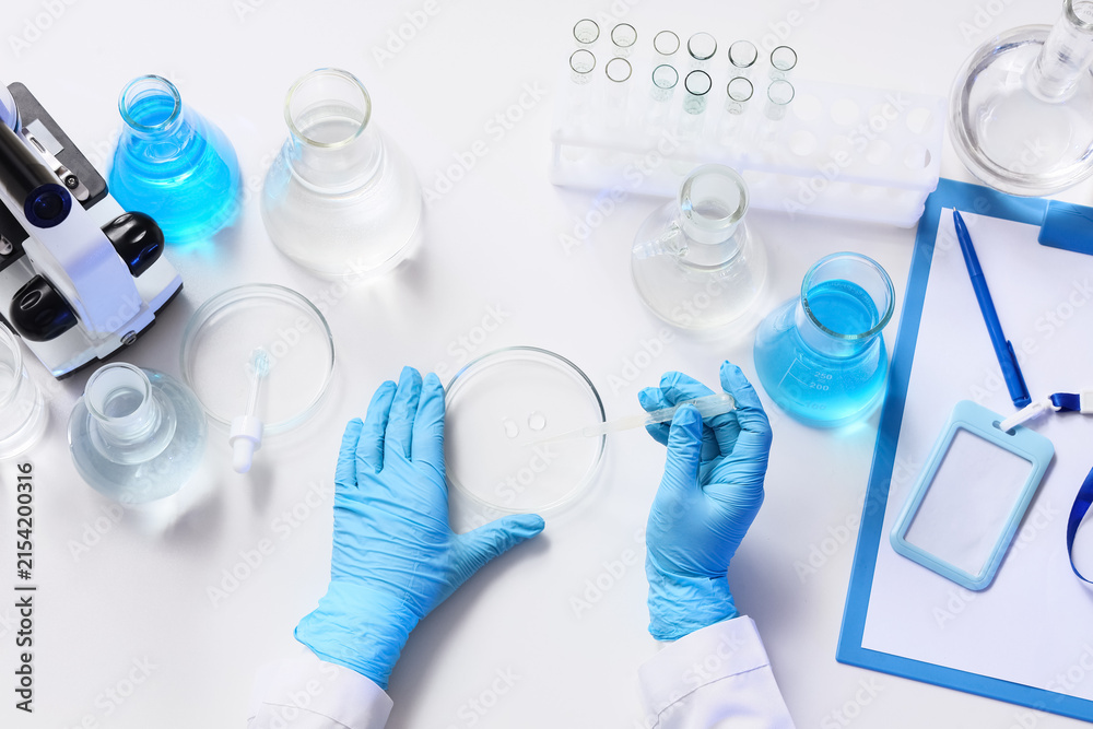 Fototapeta premium Female scientist dropping water sample onto Petri dish at table in laboratory, top view