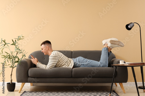 Young man using mobile phone on sofa near beige wall in living room