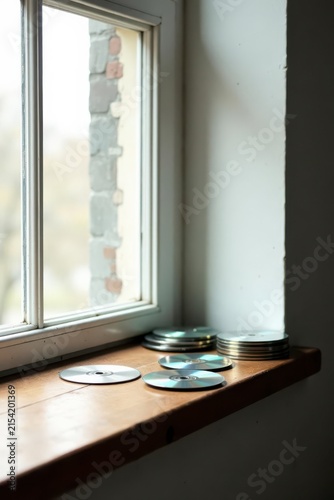 Quiet contemplation by a windowsill, stacks of data discs resting gently on aged wood, sunlight filtering through the glass panes