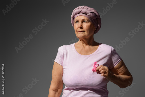 Senior woman after chemotherapy with pink ribbon on dark background. Breast c...