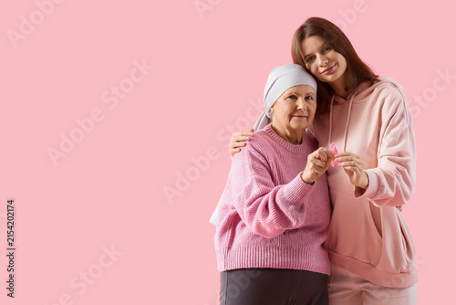 Senior woman after chemotherapy and her daughter with pink ribbon hugging on color background. Breast cancer awareness concept