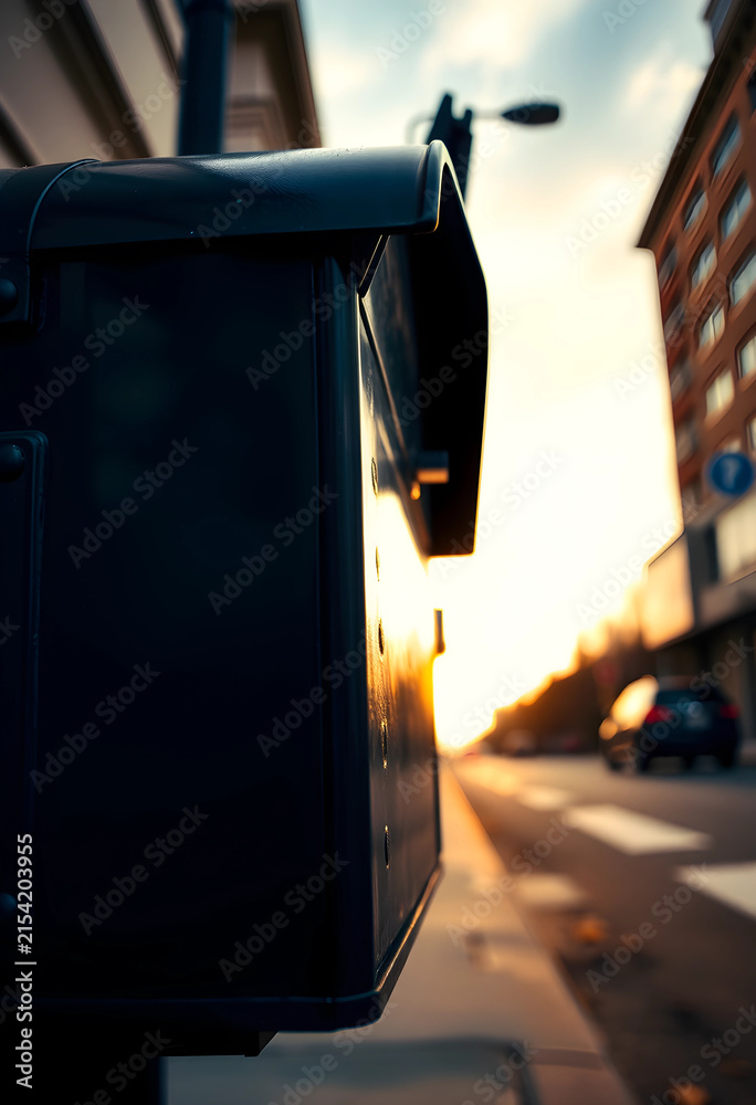 Obraz premium Dark metal mailbox on a city street at sunset with blurred background and warm light