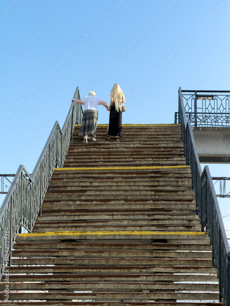 Obraz premium Two people ascend weathered stone steps under clear blue sky
